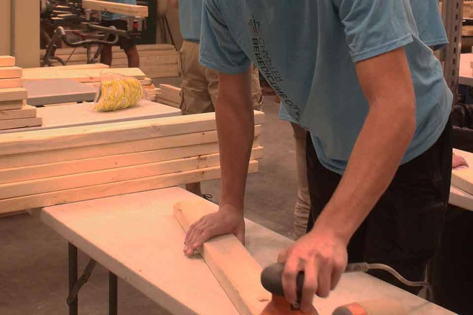 一名学生志愿者用打磨机和一块木头工作